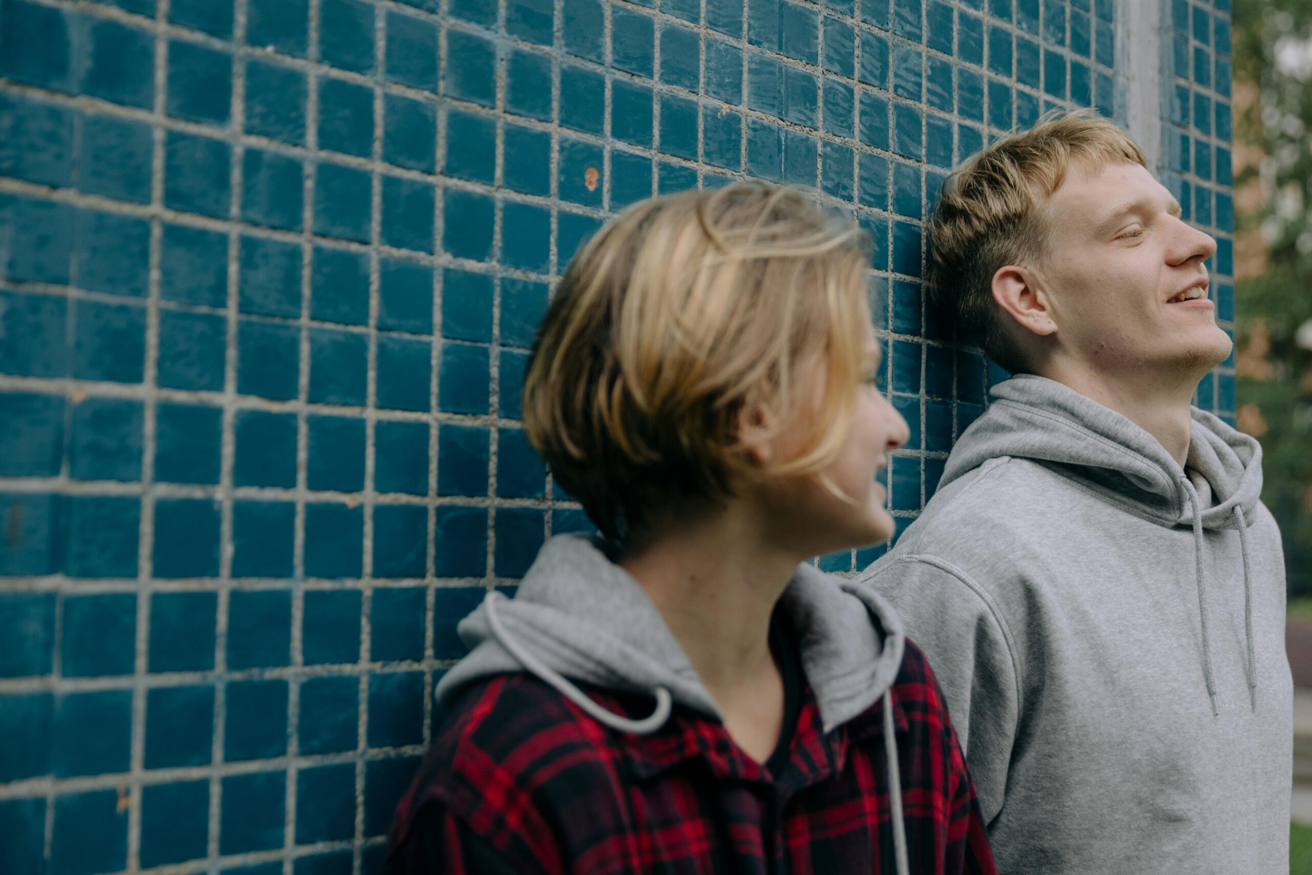 Two young adults smiling and enjoying a moment against a blue tiled wall.